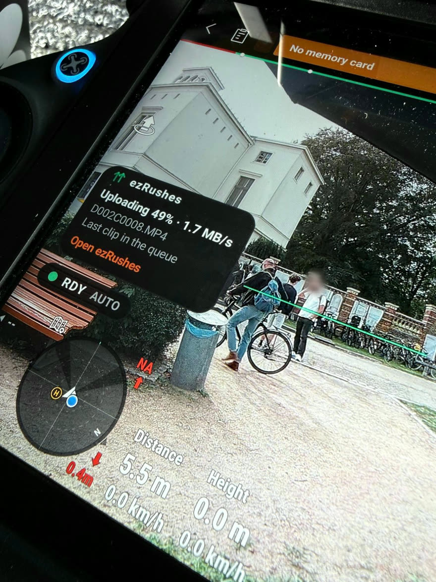 A DJI remote on set: the ezRushes status pill reads “Uploading 49% · 1.7 MB/s” over the drone’s live view.